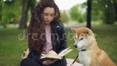 可爱的学生正在看书，坐在公园里，然后拍拍可爱的小狗，微笑着。 可爱的动物，聪明的